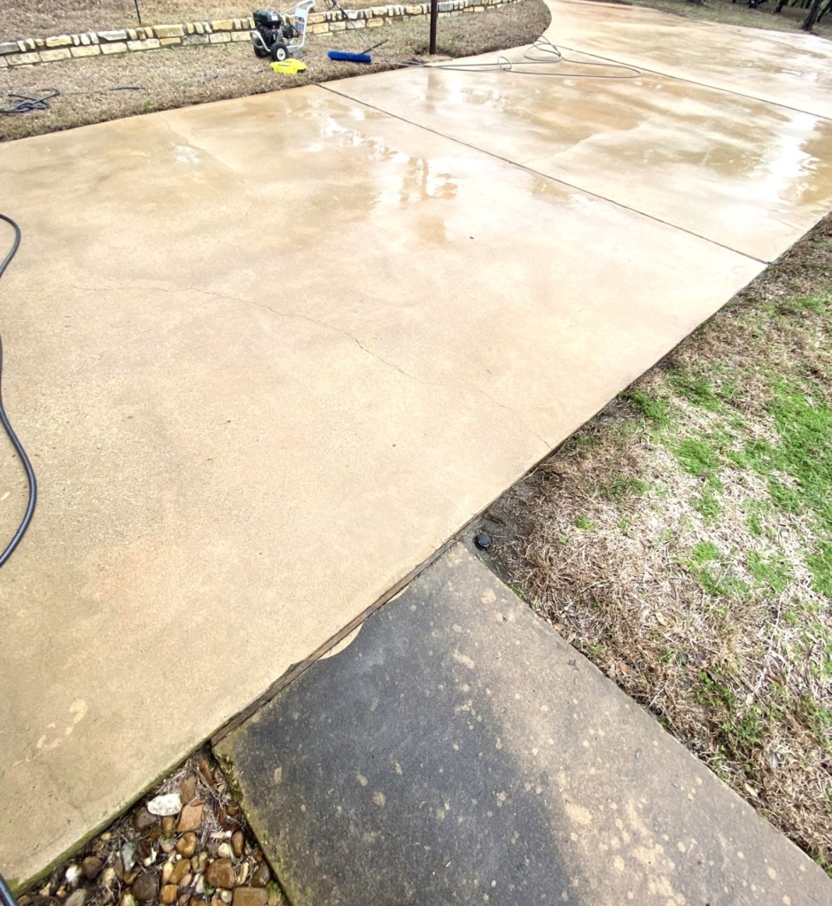 Cleaned driveway surface after pressure washing, showing a clear transition between concrete and grass.